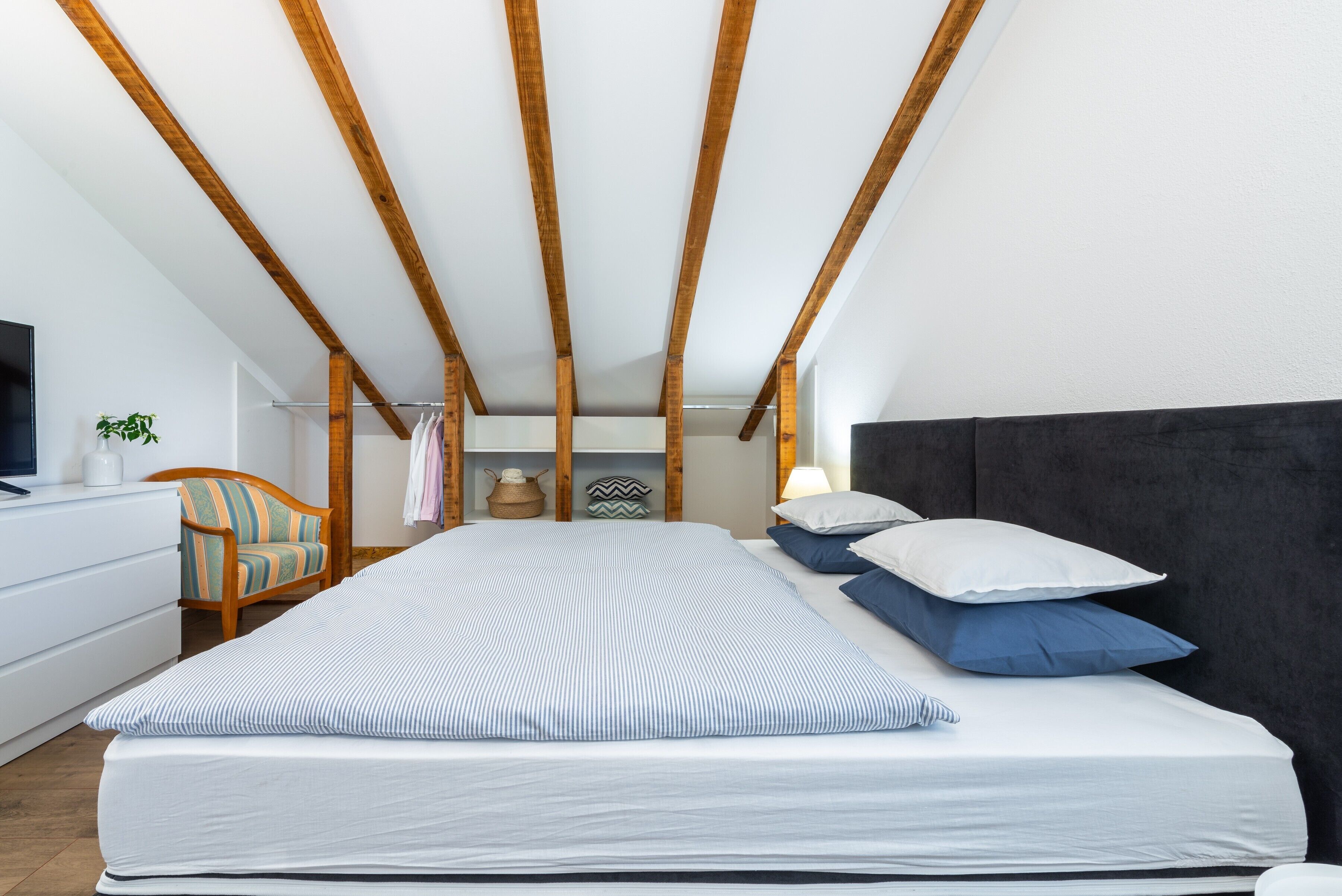 Une chambre à coucher avec un lit, des poutres en bois, une commode, une chaise et une lampe.