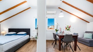 Una habitación moderna con una cama, una mesa de comedor con sillas, un sofá y una ventana con vistas a una casa.
