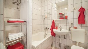 Un bagno con vasca, lavandino e servizi igienici. Sono presenti scaffali con asciugamani e una tenda da doccia.