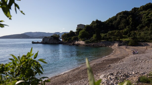 A coastal landscape with a rocky beach, clear blue water, and a building on a hillside. - Villa Dubravka - Superior One Bedroom Apartment with Balcony and Sea View (Mlini)