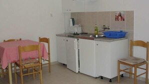 A small kitchenette with a sink, a stove, and a microwave. There is a table with a pink tablecloth and two wooden chairs. - Apartments Boguvila - One-Bedroom Apartment with Terrace (Supetar)