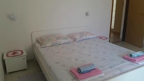 A single-bed room with a white headboard, a bedside table with a red and white object, and a window with closed blinds. - Apartments Boguvila - One-Bedroom Apartment with Terrace (Supetar)
