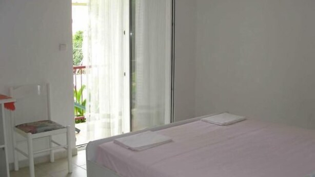 A bedroom with a bed, a chair, and a sliding glass door to a balcony. - Apartments Boguvila - One-Bedroom Apartment with Terrace (Supetar)