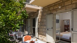 A patio with a table set for breakfast, a bed with a view, and a stone wall. - Begović Guest House - Twin Room (Judy) (Dubrovnik)