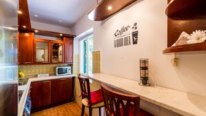A kitchen with wooden cabinets, a microwave, and a coffee station. - Apartment Valonija - Two Bedroom Apartment with Terrace and Garden View (Dubrovnik)