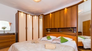 A bedroom with a large bed, wooden wardrobe, and a mirror. - Apartment Valonija - Two Bedroom Apartment with Terrace and Garden View (Dubrovnik)