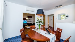 A dining area with a wooden table, chairs, a vase with flowers, and a modern pendant light. - Apartment Valonija - Two Bedroom Apartment with Terrace and Garden View (Dubrovnik)