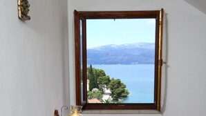 A bedroom with a bed, a nightstand with a lamp, and a window with a view of a lake and mountains. - Apartments Boro - Two Bedroom Apartment with Sea View (A2) (Splitska)