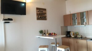 Een keuken met houten kastjes, een wit aanrecht, een barkruk, een televisie aan de muur en een bord met de tekst 'Live Love LAUGH'.