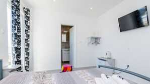 A hotel room with a bed, a TV mounted on the wall, a small desk, and a bathroom visible through an open door. - Guest House Nikolina - Double Room with Balcony and Sea View(1) (Dubrovnik)
