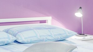 Een slaapkamer met een bed, kussens, een nachtkastje en een lamp.
