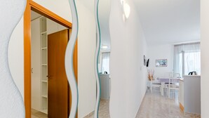 Een modern interieur met een houten deur naar een inloopkast, een eethoek met tafel en stoelen, en een keuken met een aanrecht en kasten.