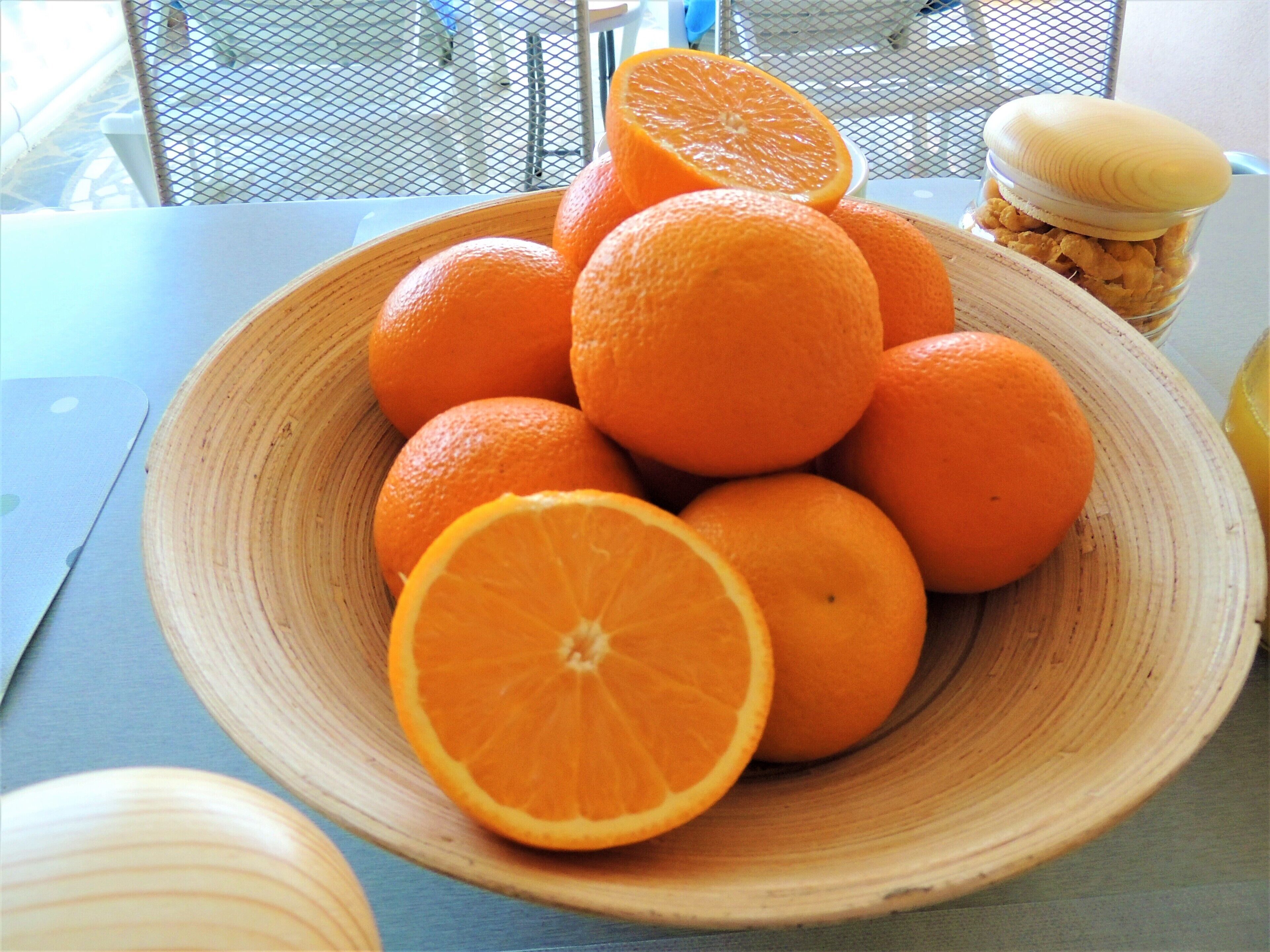A wooden bowl filled with oranges on a table.