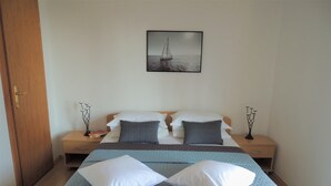 A bedroom with a bed, two bedside tables, a nightstand, a door, and a wall-mounted picture of a sailboat. - Apartment D & D Orebić - Three Bedroom Apartment with Terrace and Sea View (Orebic)