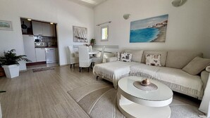 En rummelig opholdsstue med sofa, spisebord og et køkken i baggrunden.