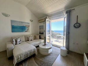 Een slaapkamer met een bank, een rond tafeltje, een bed, uitzicht op zee en een klok aan de muur.
