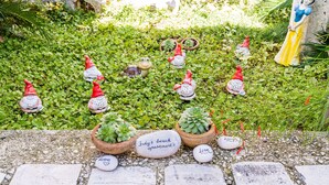 En have med forskellige dekorative statuer og planter, heriblandt en statue af Snehvide og et skilt, der står "Indy's beach apartment".