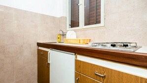 A compact kitchen with a white refrigerator, wooden cabinets, a sink, and a window with wooden shutters. - Apartments Klis -Studio Apartment with Terrace - 2 (B) (Soline)