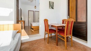 A room with a bed, a dining table with chairs, a small table with a bottle, and a door leading to another room. - Apartments Klis -Studio Apartment with Terrace - 2 (B) (Soline)