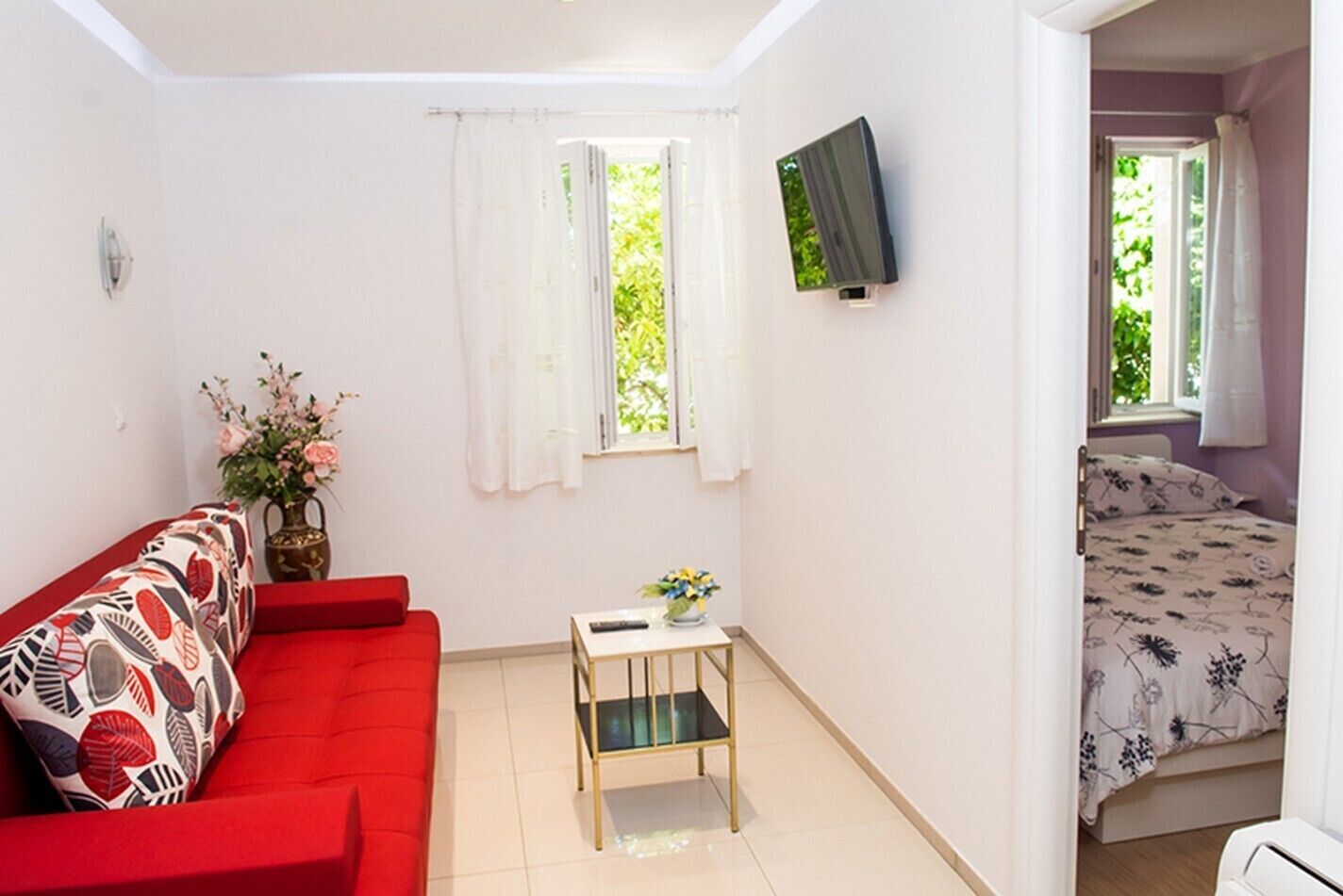 A compact room with a red sofa, a small table with a vase, and a bed with floral bedding.