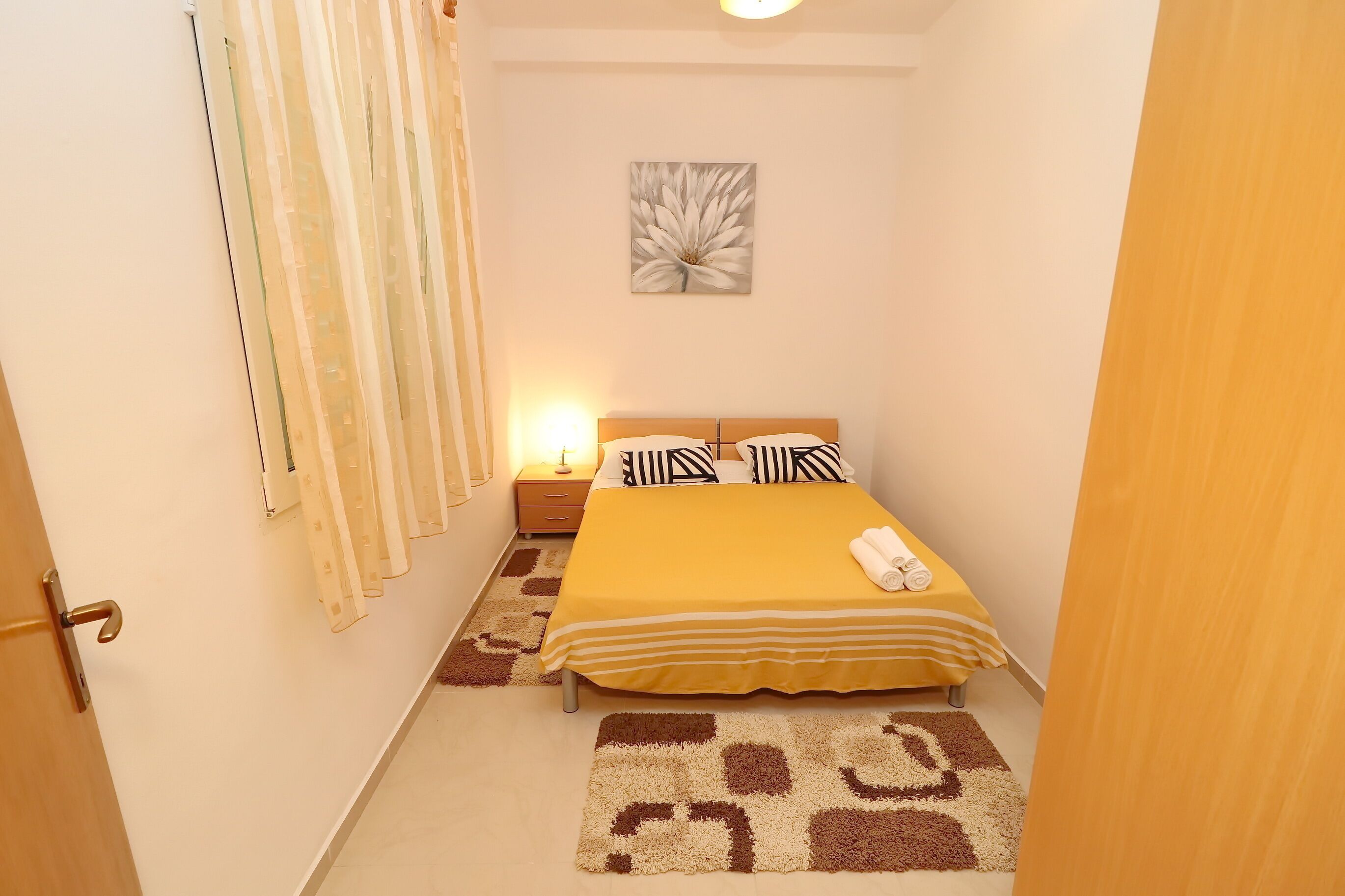 A bedroom with a bed, bedside table, lamp, and a wall-mounted artwork.