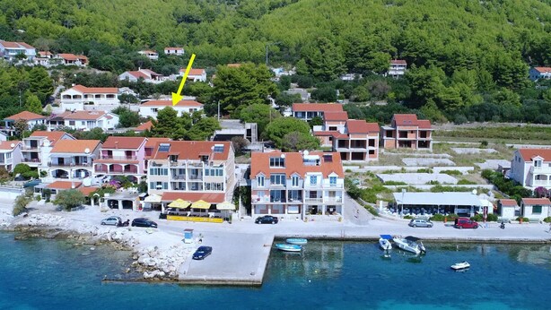 Une ville côtière avec des bâtiments le long du front de mer, une jetée où sont amarrés des bateaux et une colline en arrière-plan.