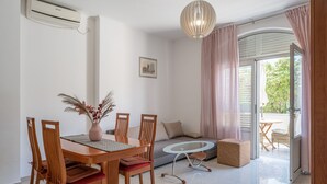 Un coin repas avec une table et des chaises en bois, une table basse avec un plateau en verre, un canapé et une petite table ronde avec des chaises à l’extérieur.