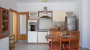 Une cuisine compacte dotée de meubles en bois, d’un four encastré, d’un réfrigérateur en acier inoxydable et d’une table à manger avec des chaises.