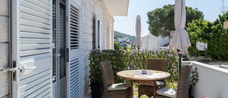 A balcony with a round table and wicker chairs, a white awning, and potted plants.