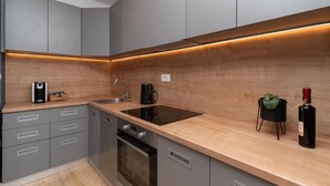 A modern kitchen with grey cabinets, a wooden countertop, a built-in oven, a sink, and a small black planter with a plant.
