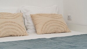A bed with two beige pillows and a blue blanket.