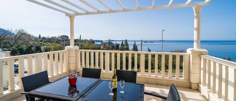 Una terraza con mesa y sillas, una botella de vino y vistas al mar.