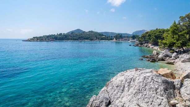 Un paisaje costero con aguas turquesas cristalinas, costas rocosas y una pequeña isla con edificios a lo lejos.