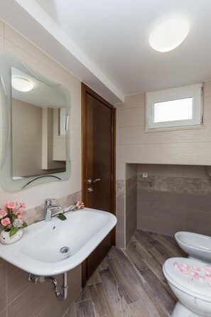 Ein Badezimmer mit weißem Waschbecken, einem Spiegel, einer Holztür, einer Duschkabine und einer Toilette.