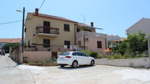A white car parked in front of a two-story building with balconies and a garden area. - Apartments Sweet Life - Three-Bedroom Apartment with Terrace and Sea view (Renata) (ST) (Supetar)