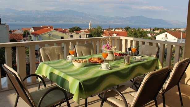 A balcony with a table set for breakfast, overlooking a coastal town and mountains. - Apartments Sweet Life - Three-Bedroom Apartment with Terrace and Sea view (Renata) (ST) (Supetar)