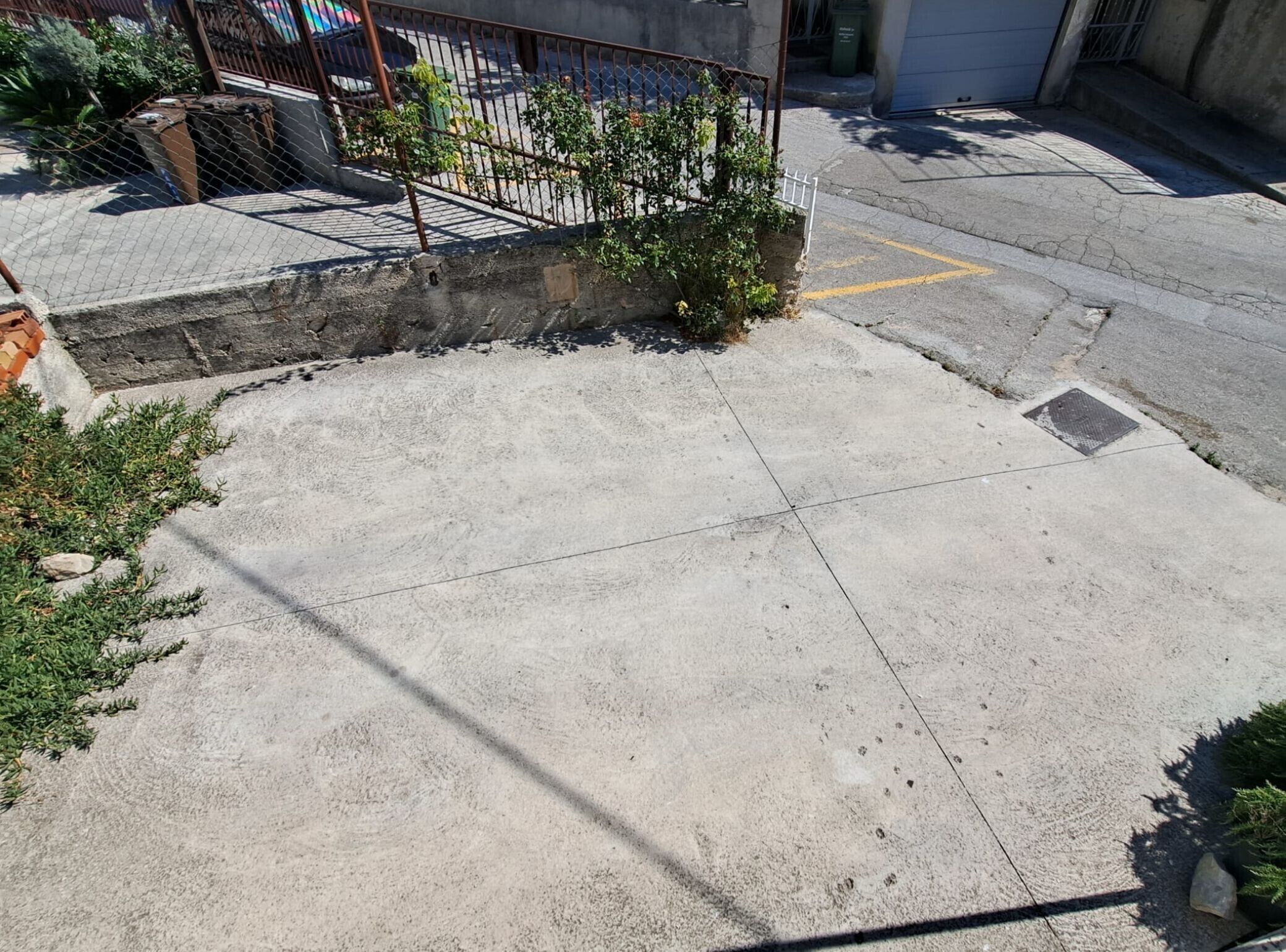 A concrete courtyard with a metal fence, a small garden area, and a visible manhole cover.