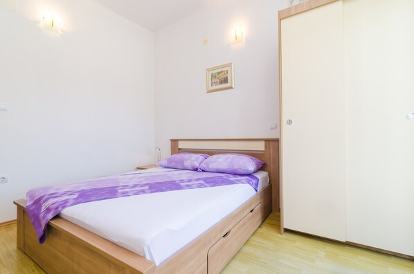 A bedroom with a bed, wooden headboard, a wardrobe, and a wall-mounted picture. - Apartments & Rooms Barišić - Standard Double Room with Balcony and Garden View (Kupari)