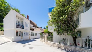 A white building with a balcony and a tree in front.