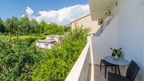 A balcony with a table and chairs, a vase with flowers, and a view of greenery and buildings.