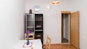 A small, sparsely furnished room with a wooden floor, a white table, a chair, a bookshelf, and a door leading to another room. - Apartments Felix Mljet - Studio with Balcony (Felix) (Babino Polje)
