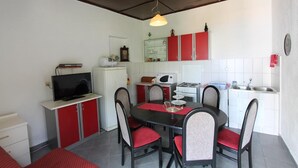 A compact kitchen with red cabinets, a microwave, and a sink. There is a dining table with chairs and a television on a cabinet. - Apartments Cervelin - Two-Bedroom Apartment with Two Terraces and Sea View (Lopud)