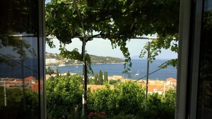 A view through a window with a view of a coastal landscape, including buildings and a body of water. - Apartments Cervelin - Two-Bedroom Apartment with Two Terraces and Sea View (Lopud)
