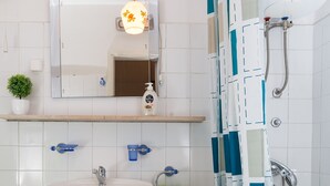 Un baño con lavamanos blanco, espejo y zona de ducha.