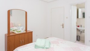 Une chambre d’hôtel avec un lit, une armoire en bois, un miroir, une porte et une salle de bain visible à travers une porte ouverte.