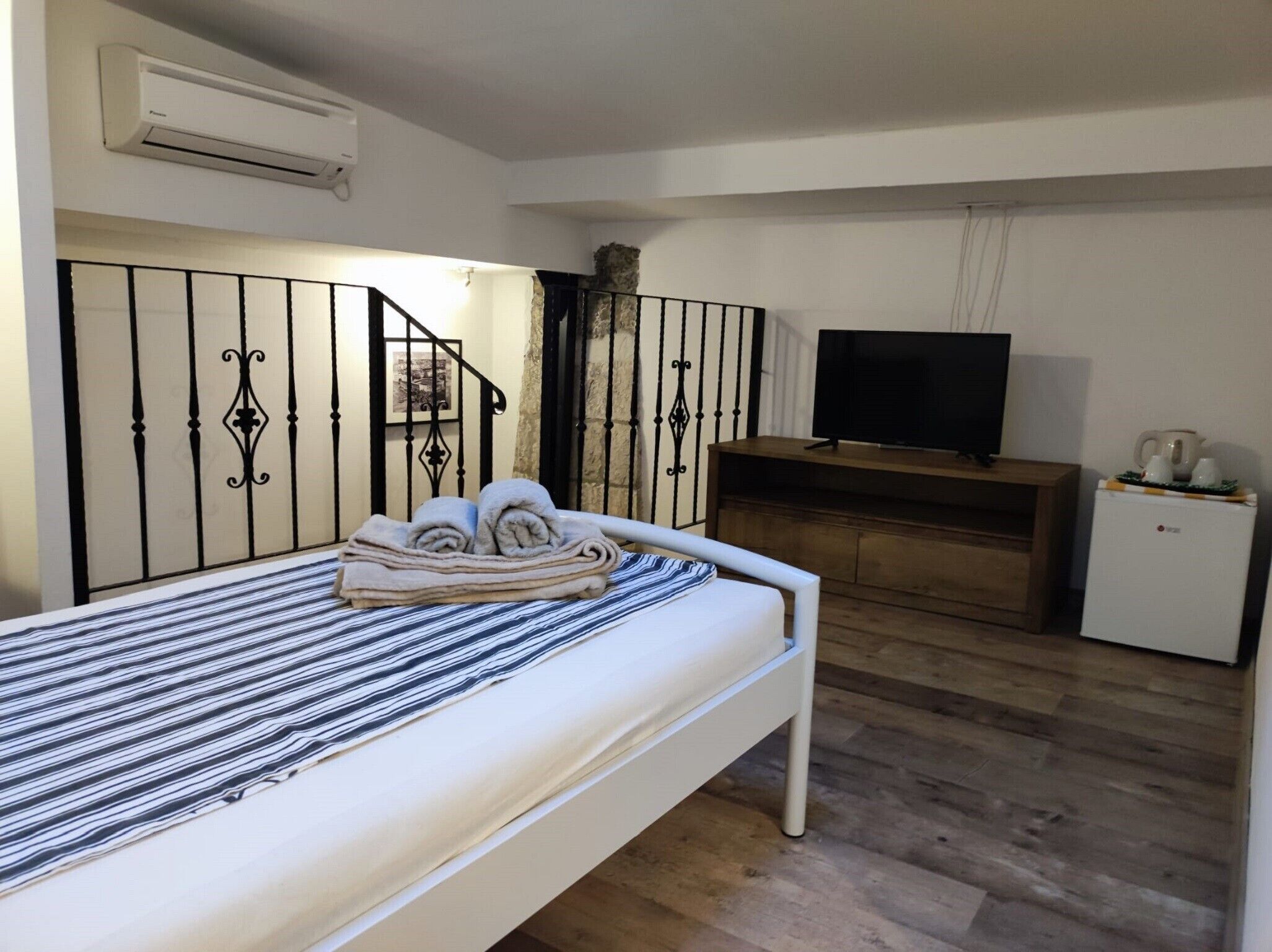Un dormitorio con cama, televisión, un mueble pequeño y un equipo de aire acondicionado.