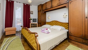 Een slaapkamer met een bed, een houten garderobe, een klein tafeltje met een televisie en een bankje.