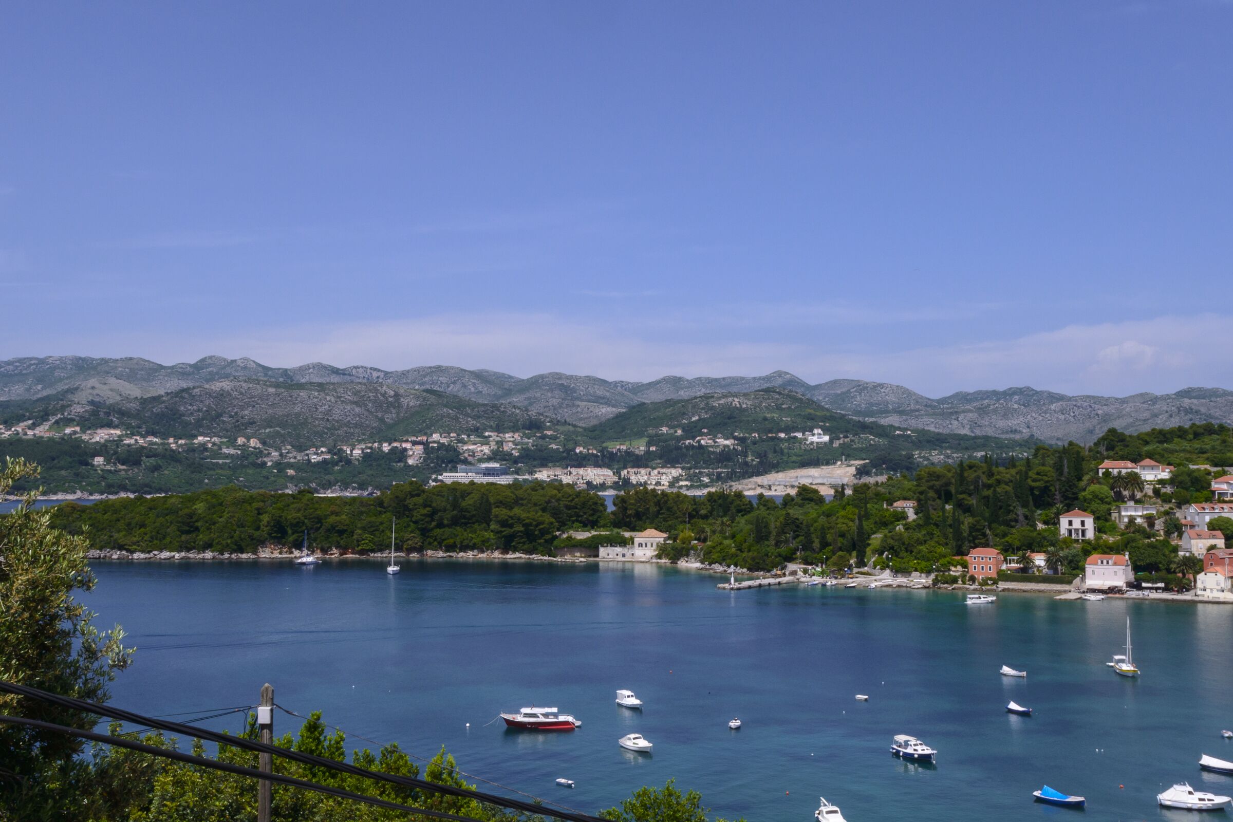 A coastal town with boats on a calm sea, surrounded by mountains and greenery.