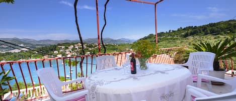 A round table with a white tablecloth and chairs with pink and white cushions, set on a balcony overlooking a body of water and a mountainous landscape.