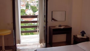 Quarto de hotel com varanda, uma cama, uma escrivaninha e uma mesa de cabeceira.